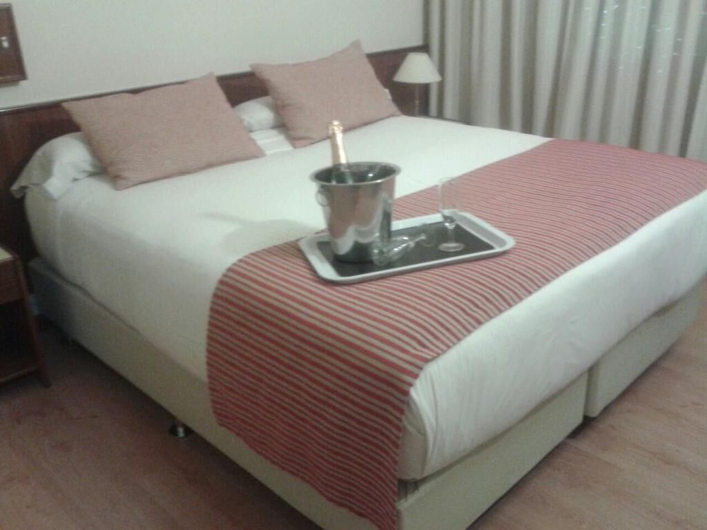 Une chambre d’hôtel avec un lit, une table de chevet, une lampe, une bouteille de champagne et un plateau avec un verre.