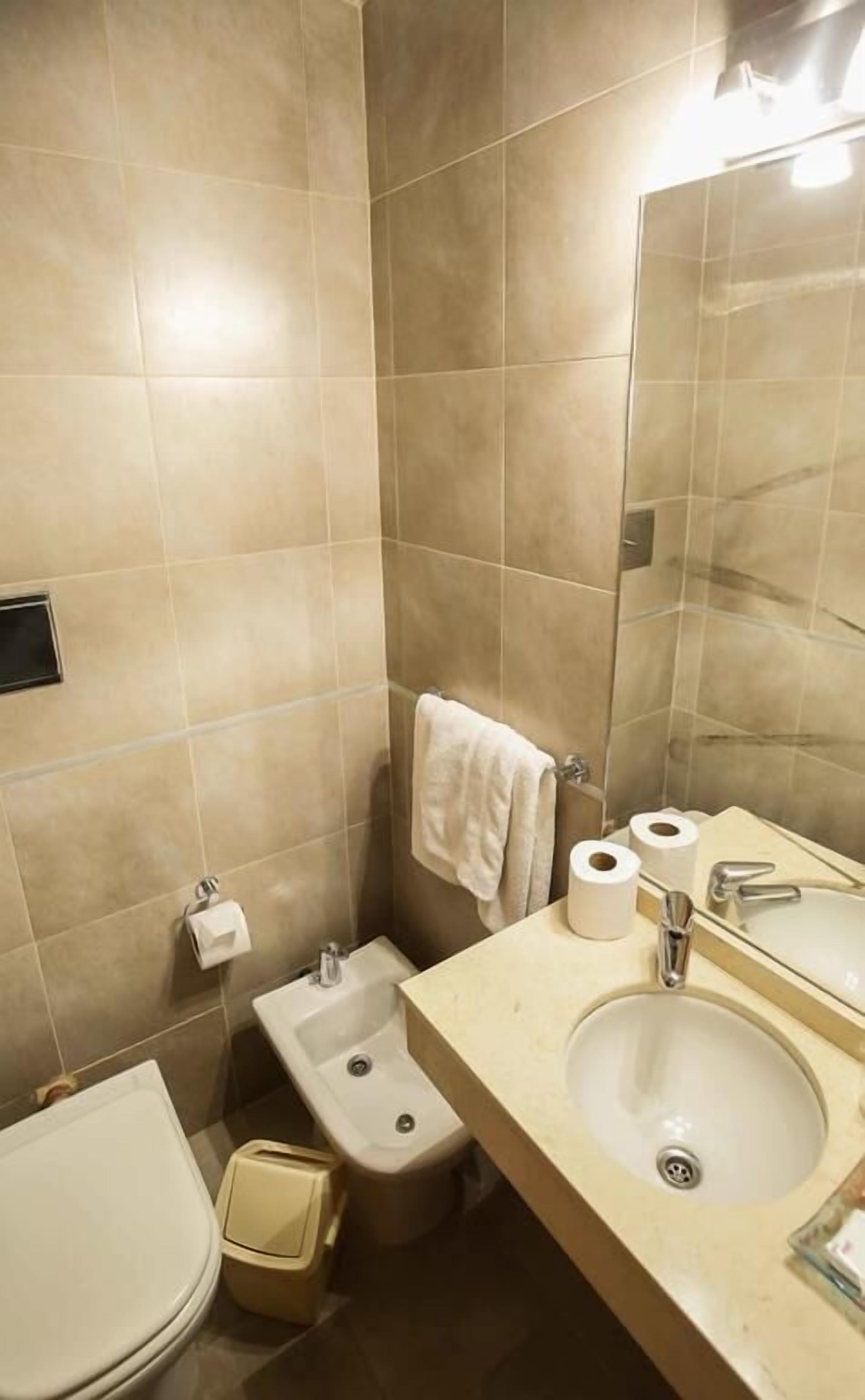Un bagno con piastrelle color beige, un lavandino, un bidet, un water e uno specchio.