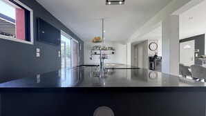 A modern kitchen with a black countertop, a built-in oven, and a stainless steel range hood. - Spacious Retreat for 12 With Spa Option (Saint-Mars-d'Outille)
