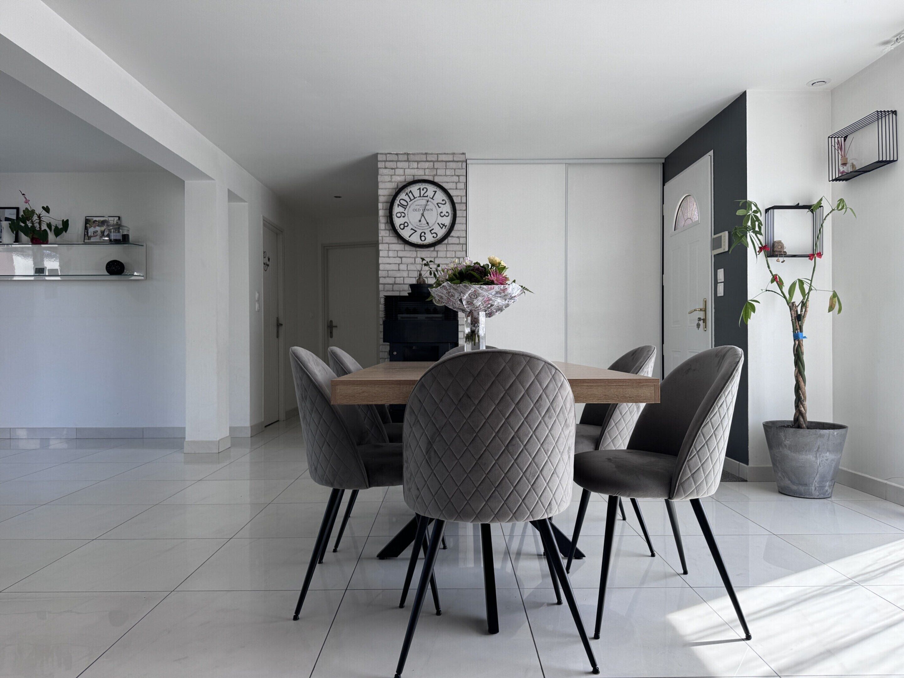 Un comedor moderno con una mesa de madera, sillas tapizadas en gris y un reloj negro en la pared.