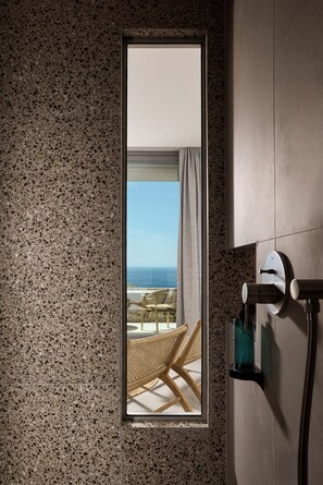 Une salle de bain avec un mur en granit, une fenêtre donnant sur l’océan, un porte-serviettes et une pomme de douche.
