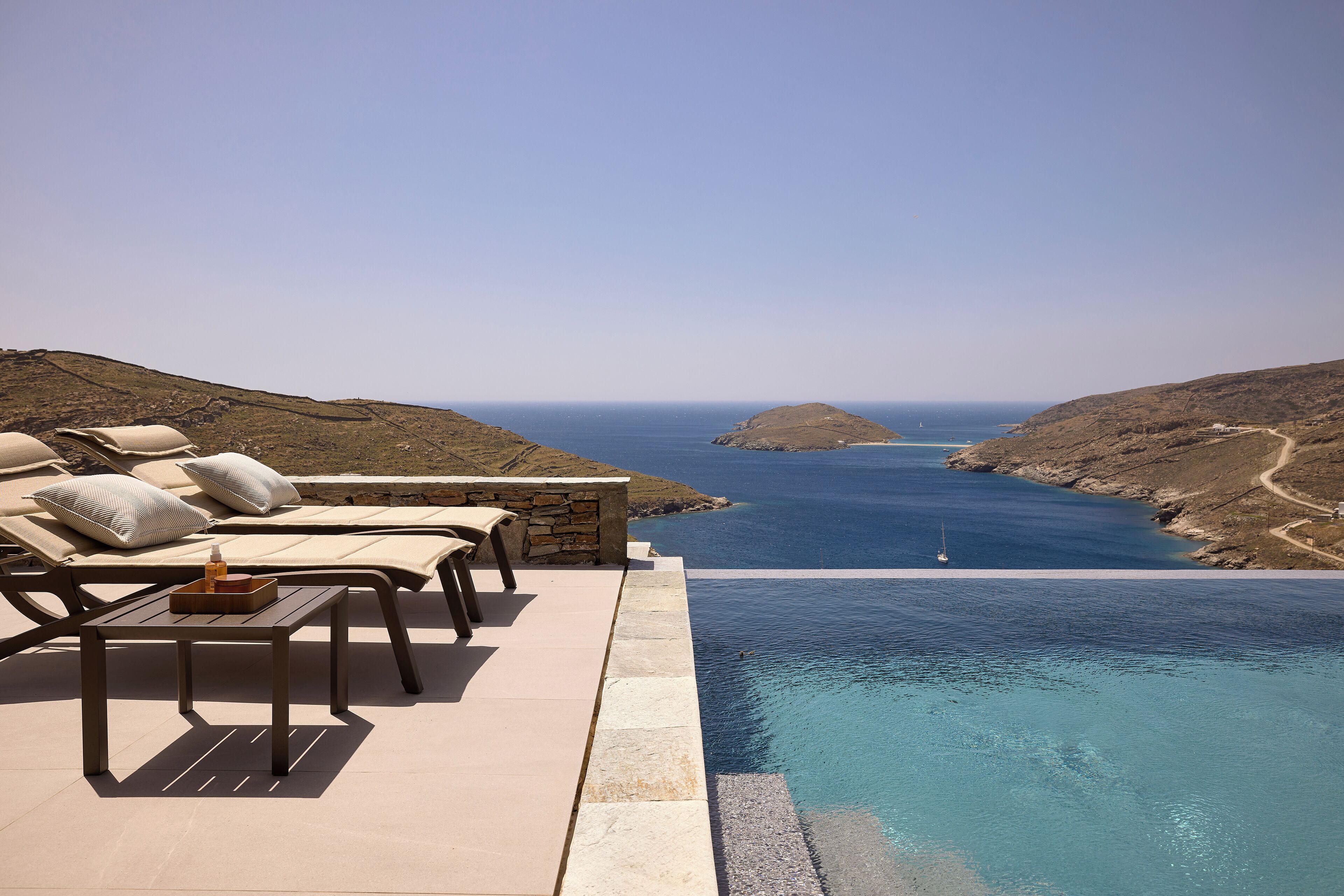 A infinity pool with a view of the sea, lounge chairs, and a table with a bottle.