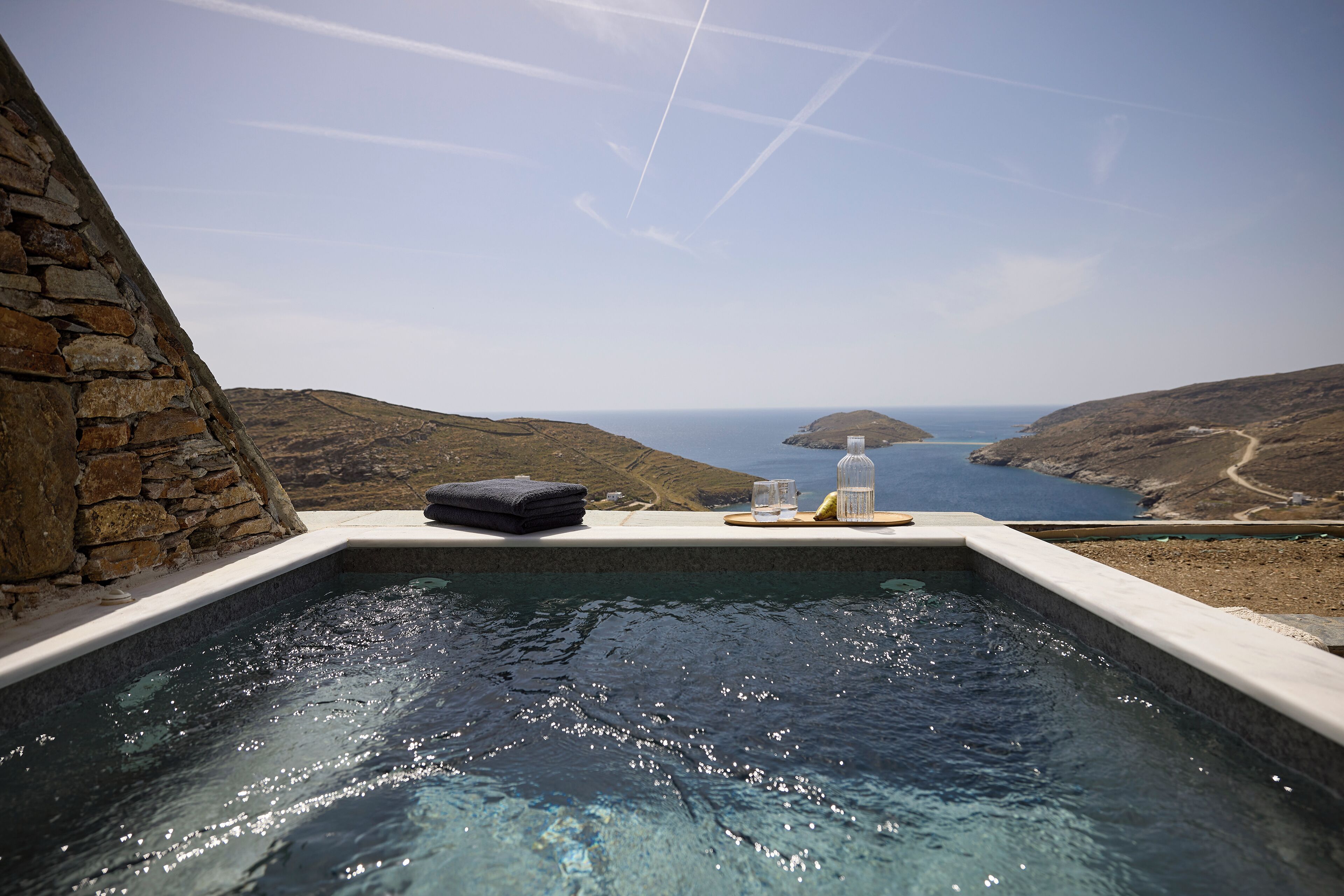 A hot tub with a stone wall and a view of the sea.