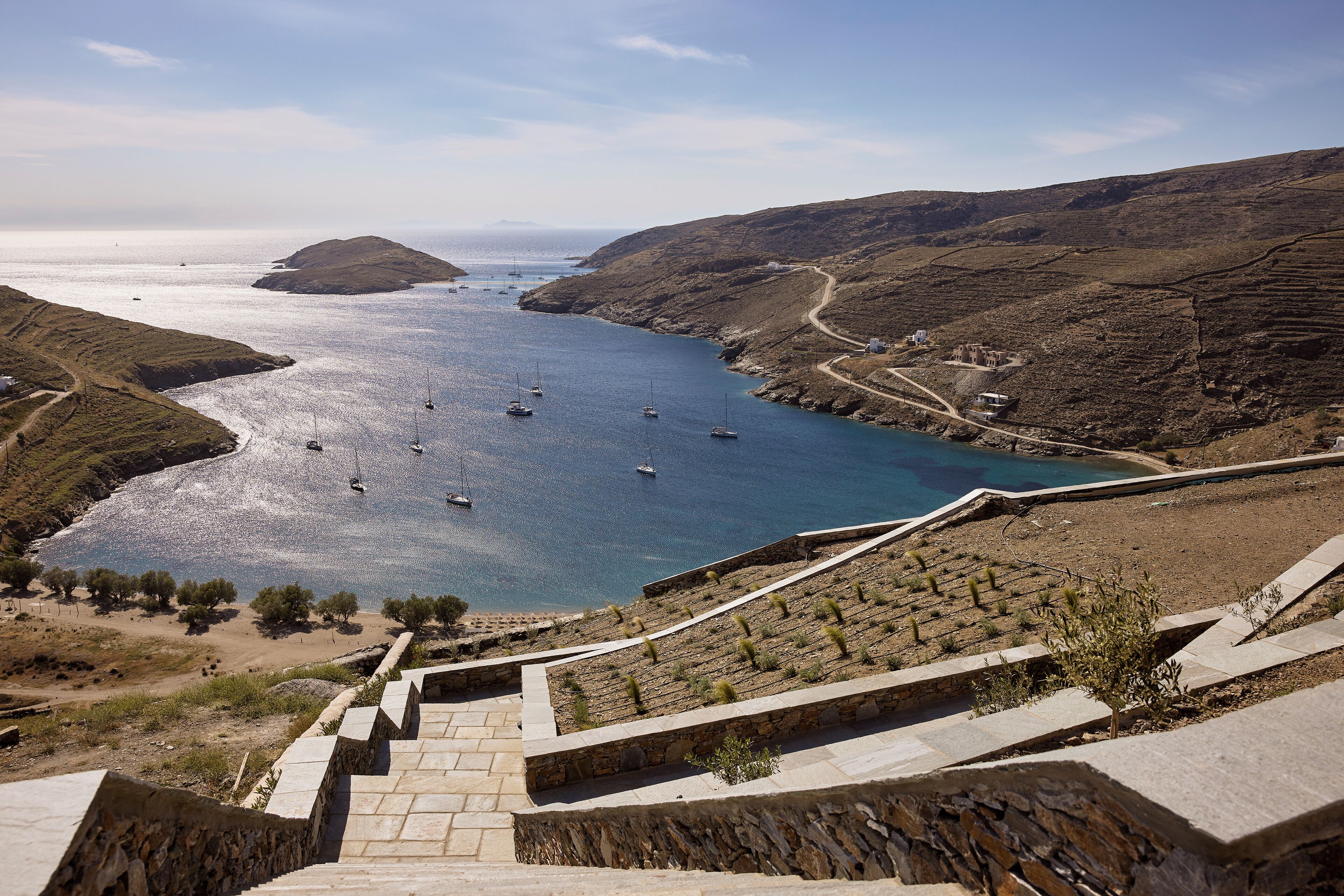 A coastal landscape with a stone staircase leading down to a beach, boats in the water, and terraced fields.