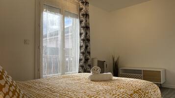 A bedroom with a bed, a bedside table, a lamp, a window with curtains, and a ceiling light.