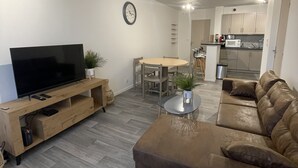 Un salon moderne doté d’un téléviseur à écran plat, d’un canapé en cuir marron, d’une table basse en bois et d’un coin repas avec une table et des chaises.