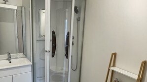 Une salle de bain avec une douche à parois de verre, un lavabo blanc et une étagère en bois.