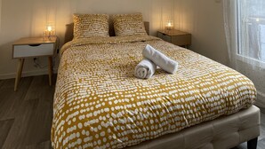 Une chambre à coucher comprenant un lit, deux tables de chevet, une fenêtre avec des rideaux et un luminaire au plafond.