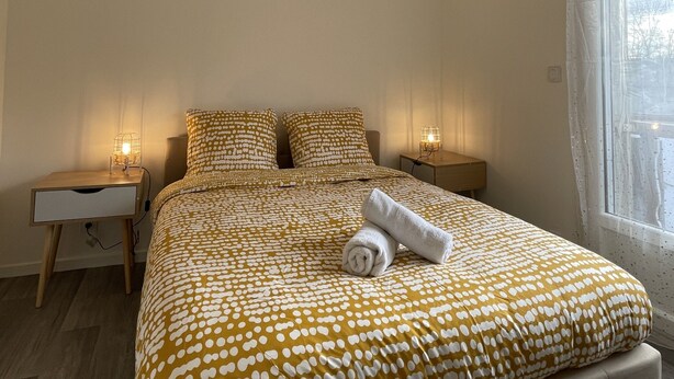 Une chambre à coucher comprenant un lit, deux tables de chevet, une fenêtre et un luminaire au plafond.