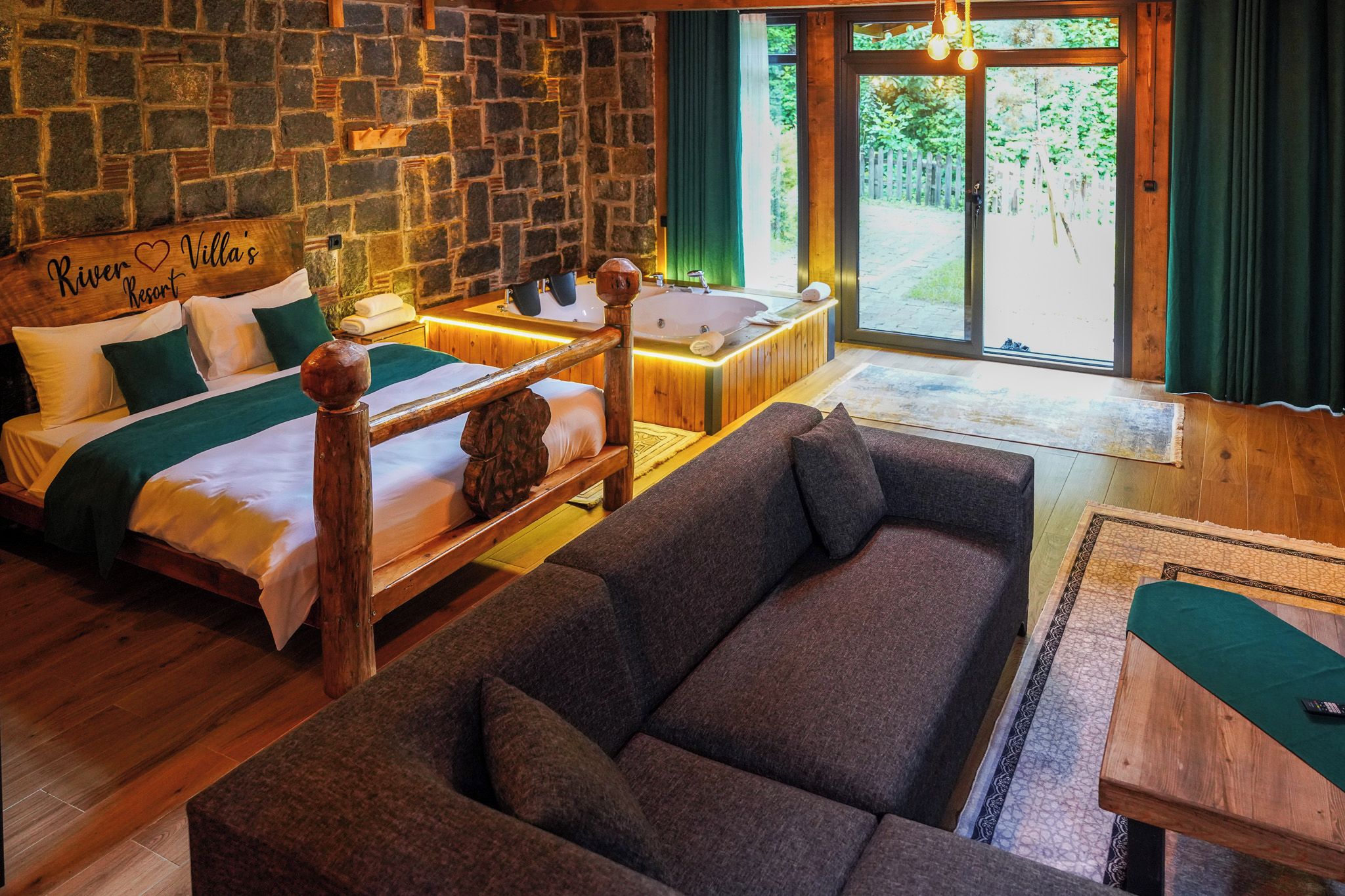 Une pièce avec un mur en pierre, un lit avec une tête de lit en bois, un canapé et une fenêtre avec des rideaux.