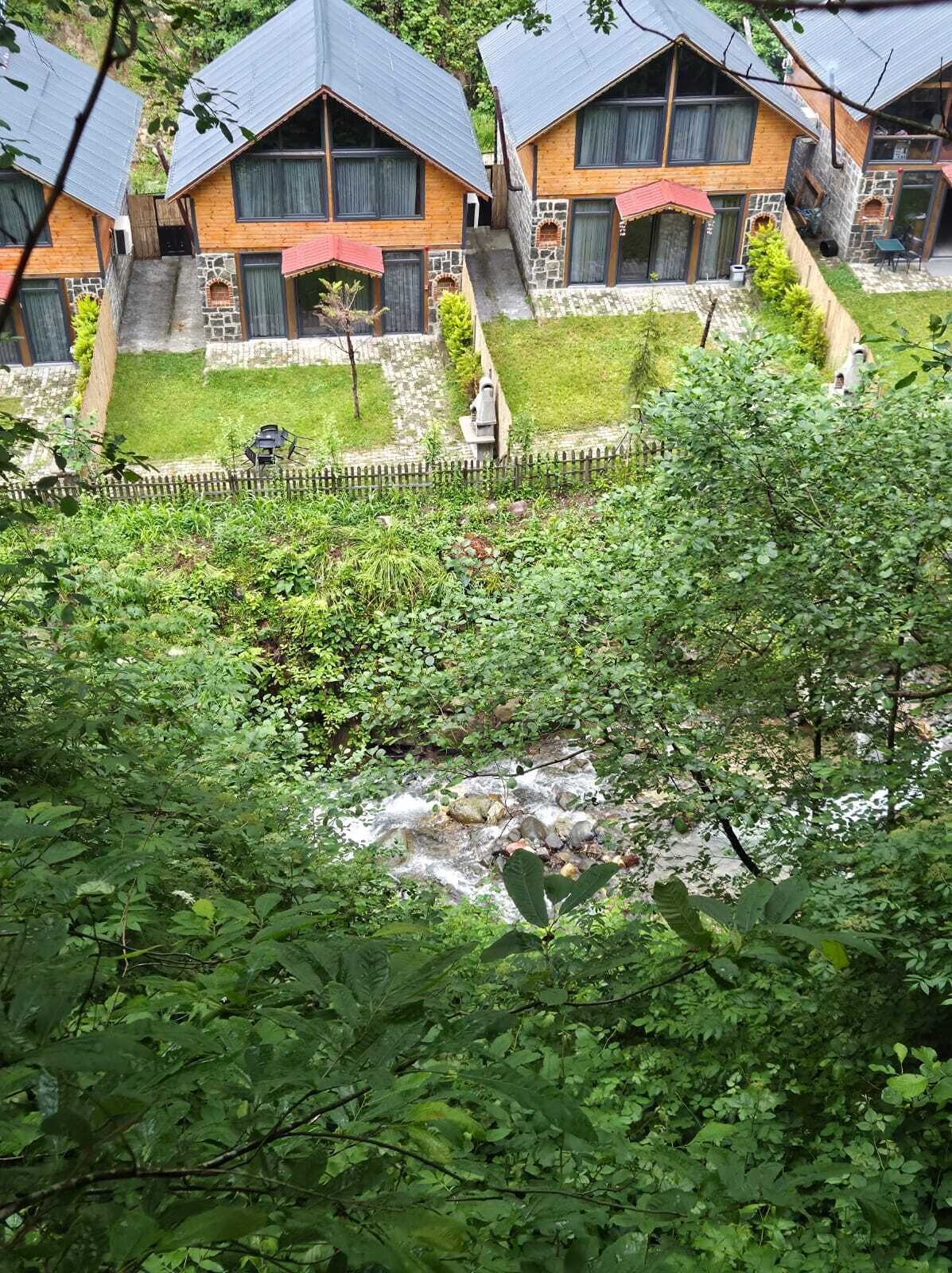 A row of wooden cabins with stone accents, a stone staircase, and a small stream in the foreground.