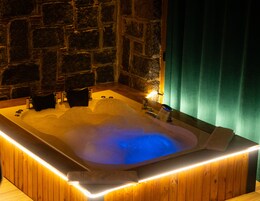 Uma banheira de hidromassagem com estrutura de madeira e parede de pedra ao fundo.