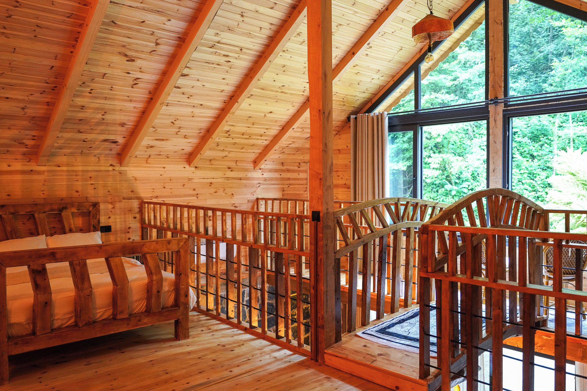 Ein Holzhütten-Interieur mit einem Bett, Sesseln und einem großen Fenster mit Blick ins Freie.