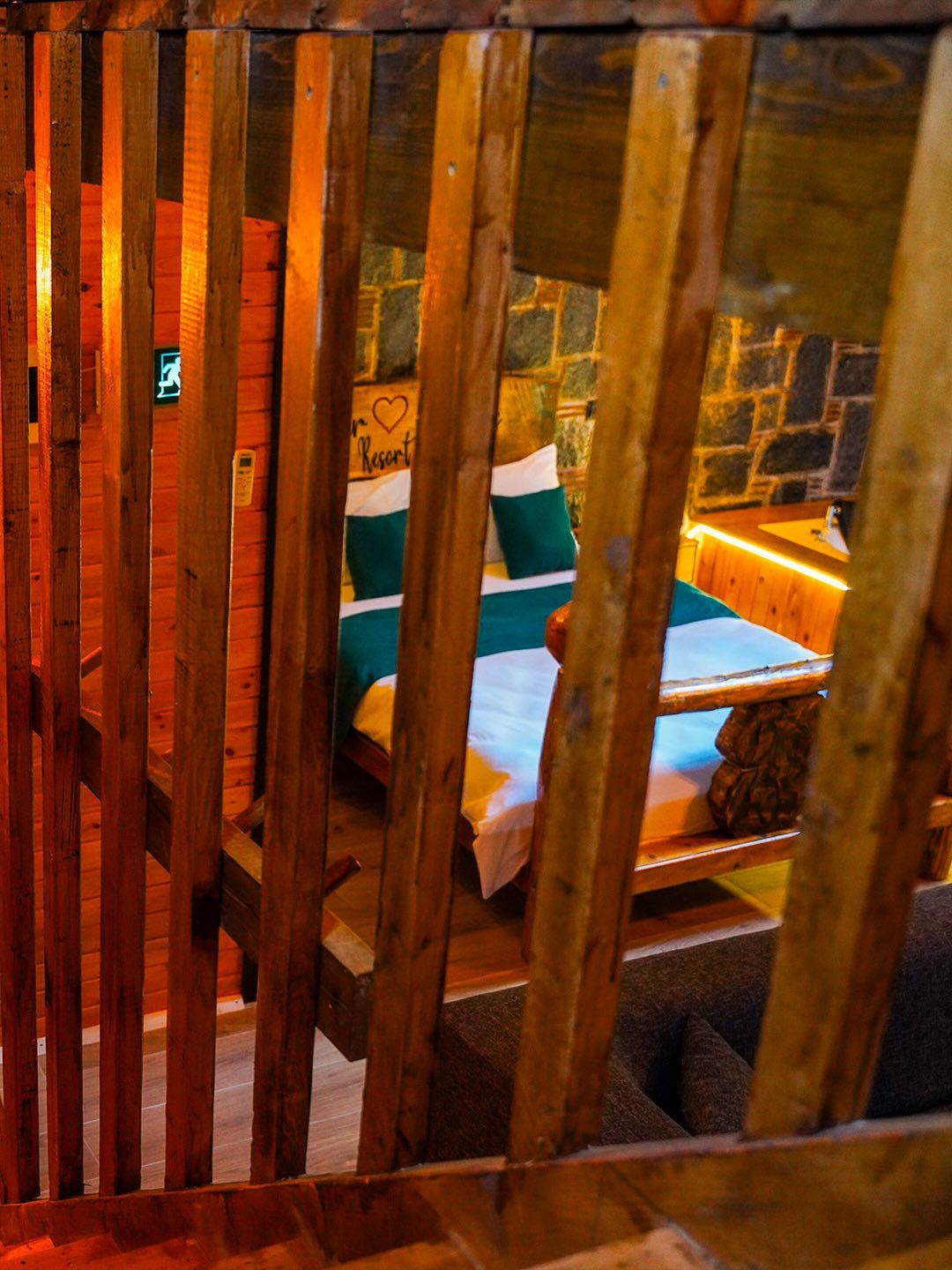 A wooden-framed room with a bed, a stone wall, and a sign indicating a heart symbol.
