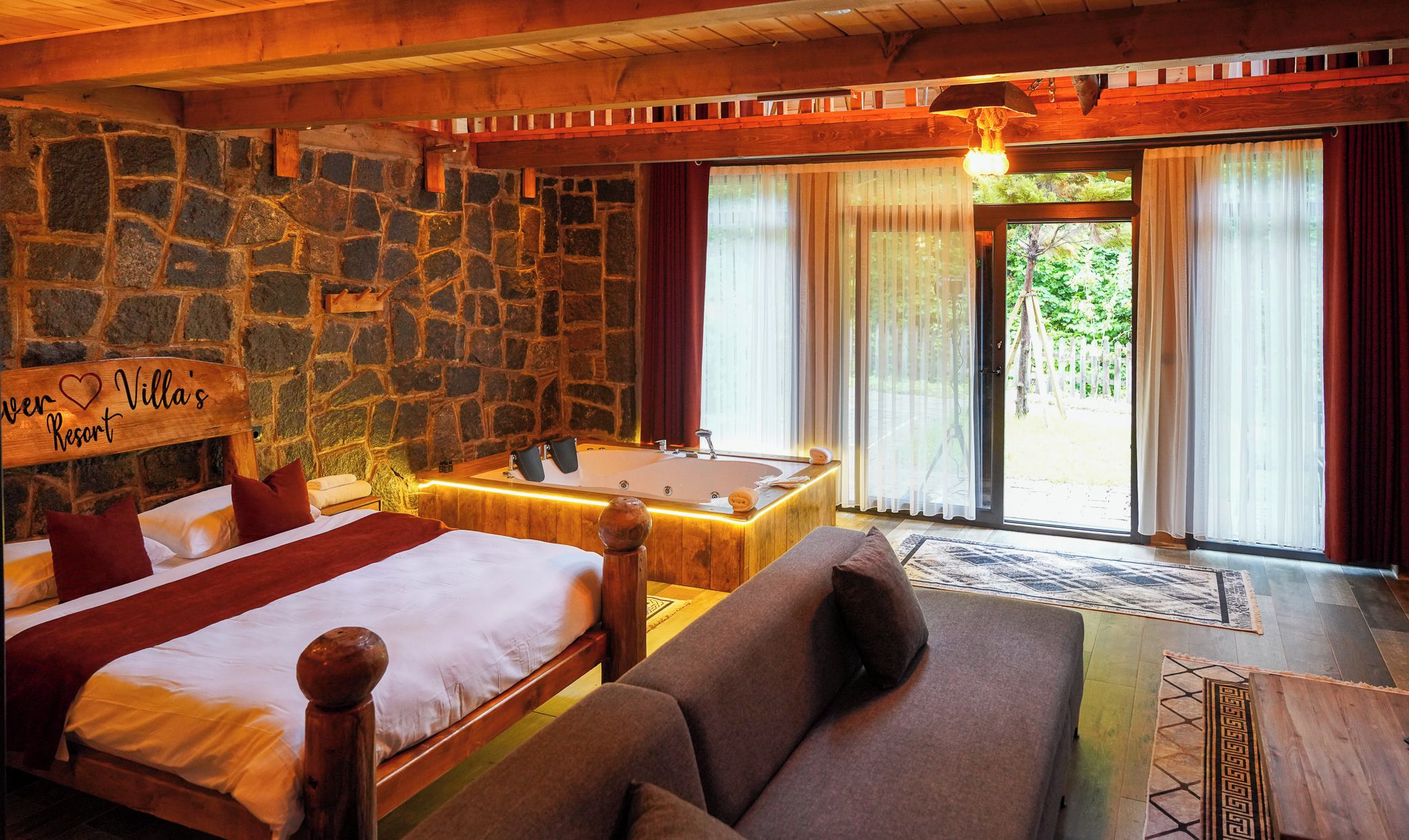 A bedroom with a stone wall, a large bed, a sofa, and a bathtub.