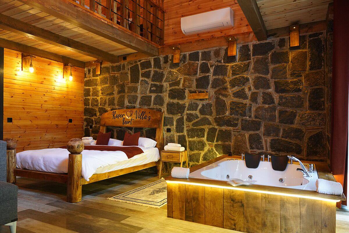 A cozy room with two wooden beds, a stone wall, and a wooden bathtub with a towel.