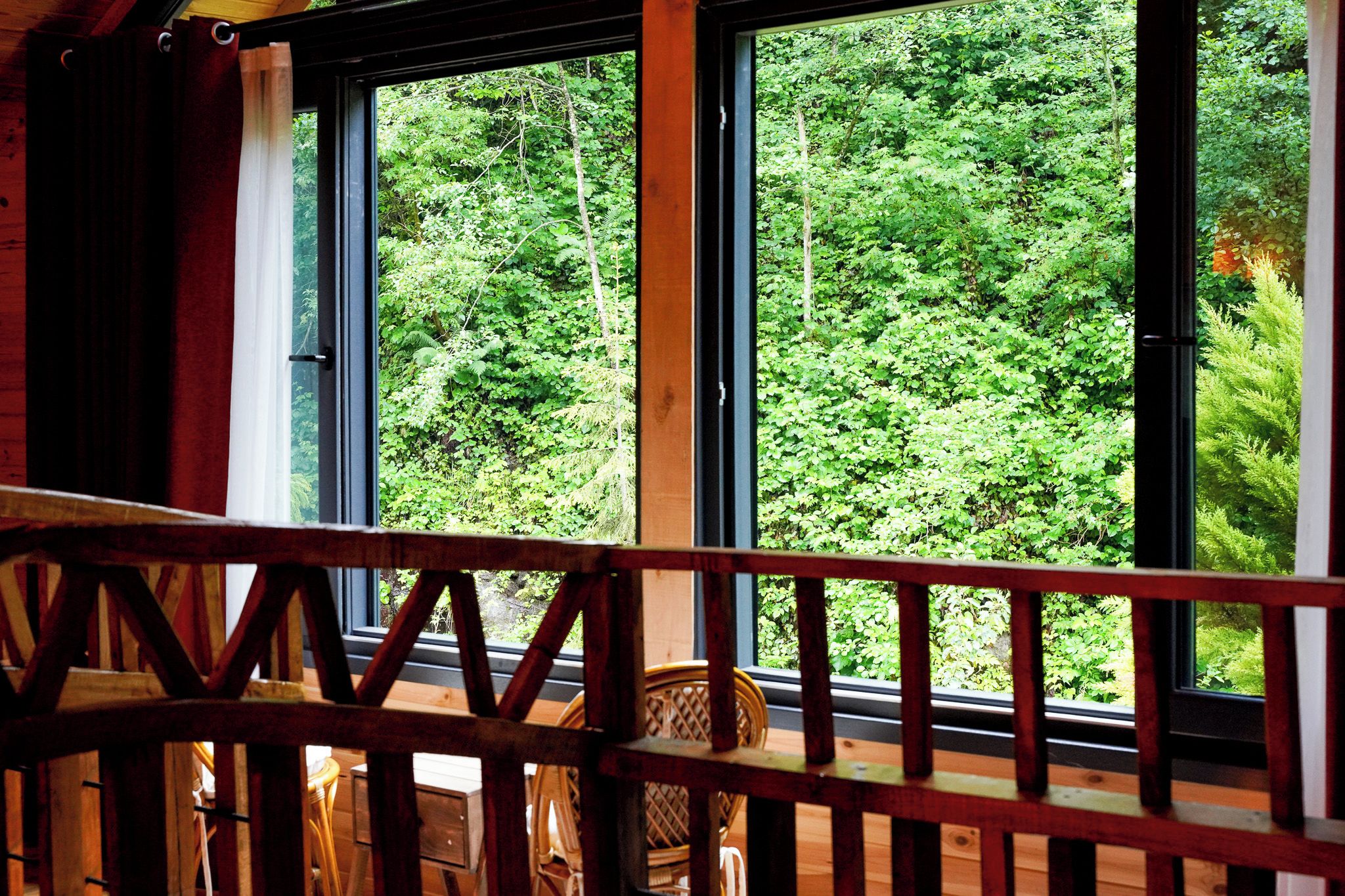 A wooden balcony with a view of dense green foliage through large windows.