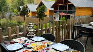 An outdoor dining area with a variety of food and drinks, surrounded by wooden cabins and a wooden fence.