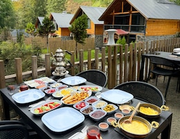 An outdoor dining area with a variety of food and drinks, surrounded by wooden cabins and a wooden fence.