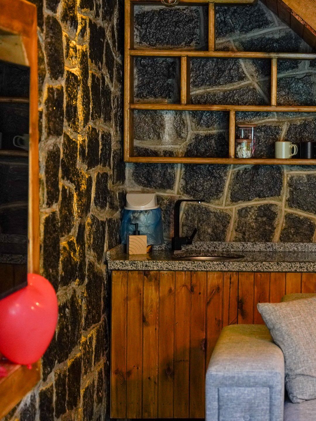 A stone wall with a built-in shelf, a wooden bench, and a red balloon.