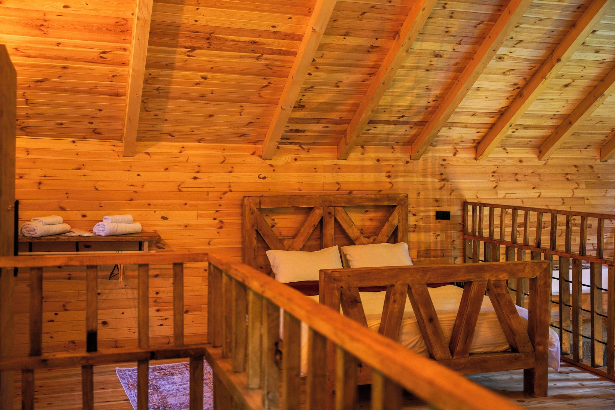 A wooden cabin interior with a bed, a bench with towels, and a railing.