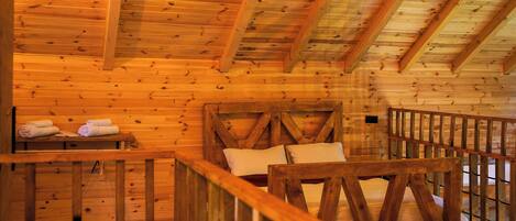 A wooden cabin interior with a bed, a bench with towels, and a railing.