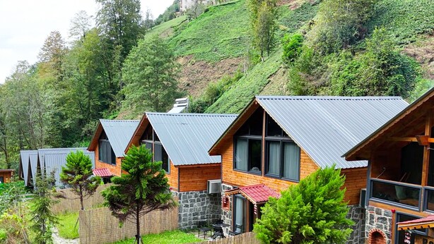 A row of wooden cabins with metal roofs, stone walls, and a stone fireplace in the foreground.