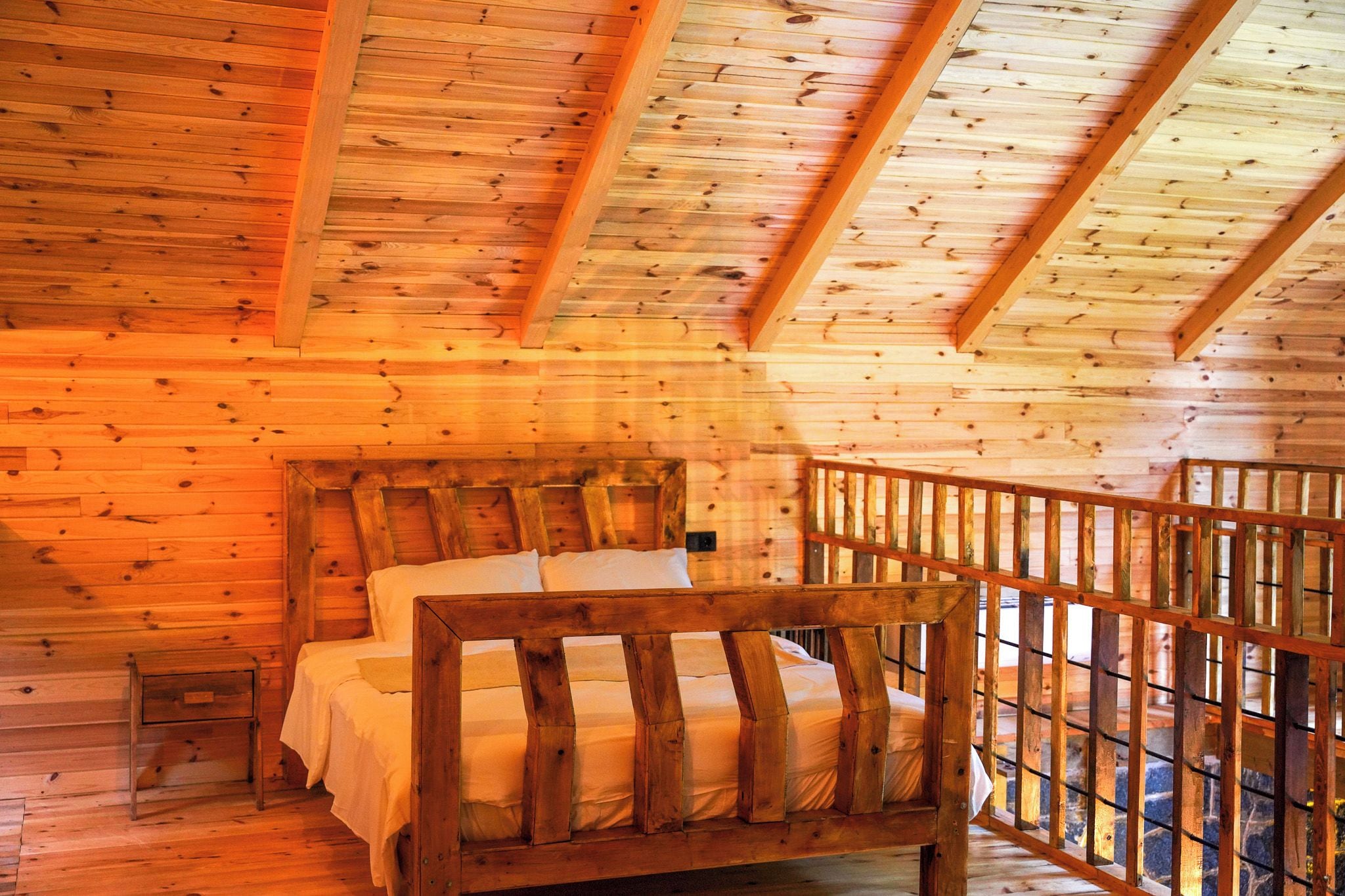 Ein Holzblockhaus im Inneren mit einem Bett, einem kleinen Nachttisch und einer Holzbalkonage.