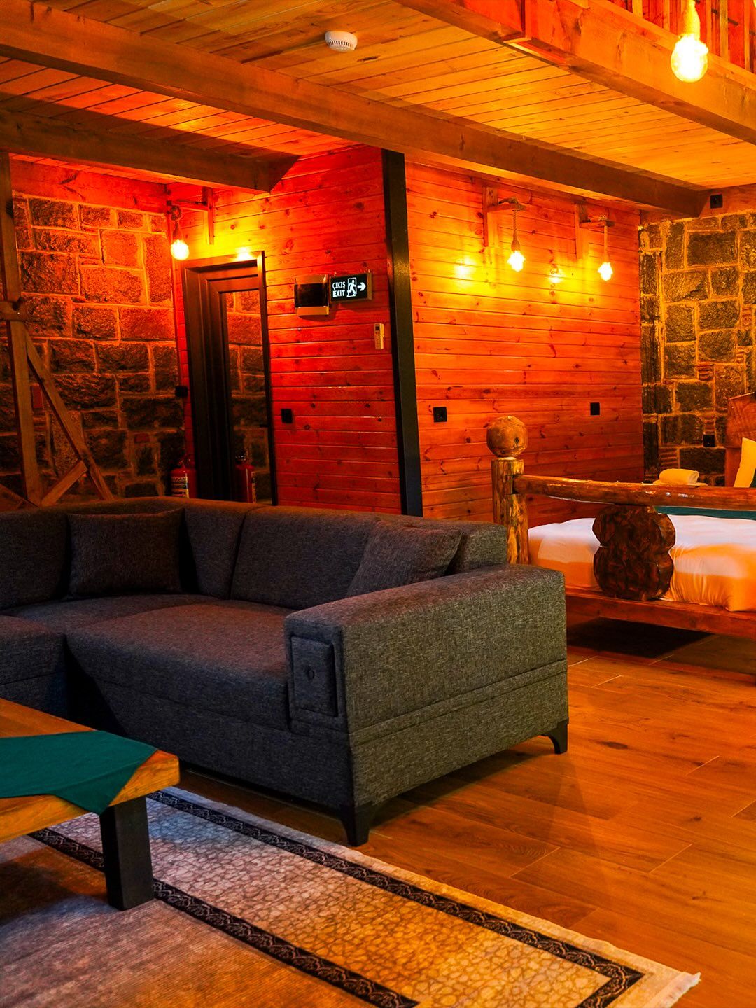 A cozy room with a sofa, a bed, a stone wall, and a wooden ceiling.