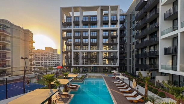 Un bâtiment moderne doté d’une piscine sur le toit, de nombreux balcons et d’un court de tennis.