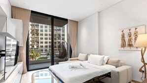 Une chambre d’hôtel moderne équipée d’un lit, d’un canapé, d’un fauteuil, d’une télévision et d’une grande fenêtre donnant sur des immeubles.