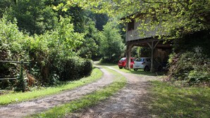 A rural road with a wooden structure on the right and two cars parked nearby. - Atelier du Moulin all in wood classified 2 * for 2 to 4 pers - on the banks of the torrent (Aubusson-d'Auvergne)