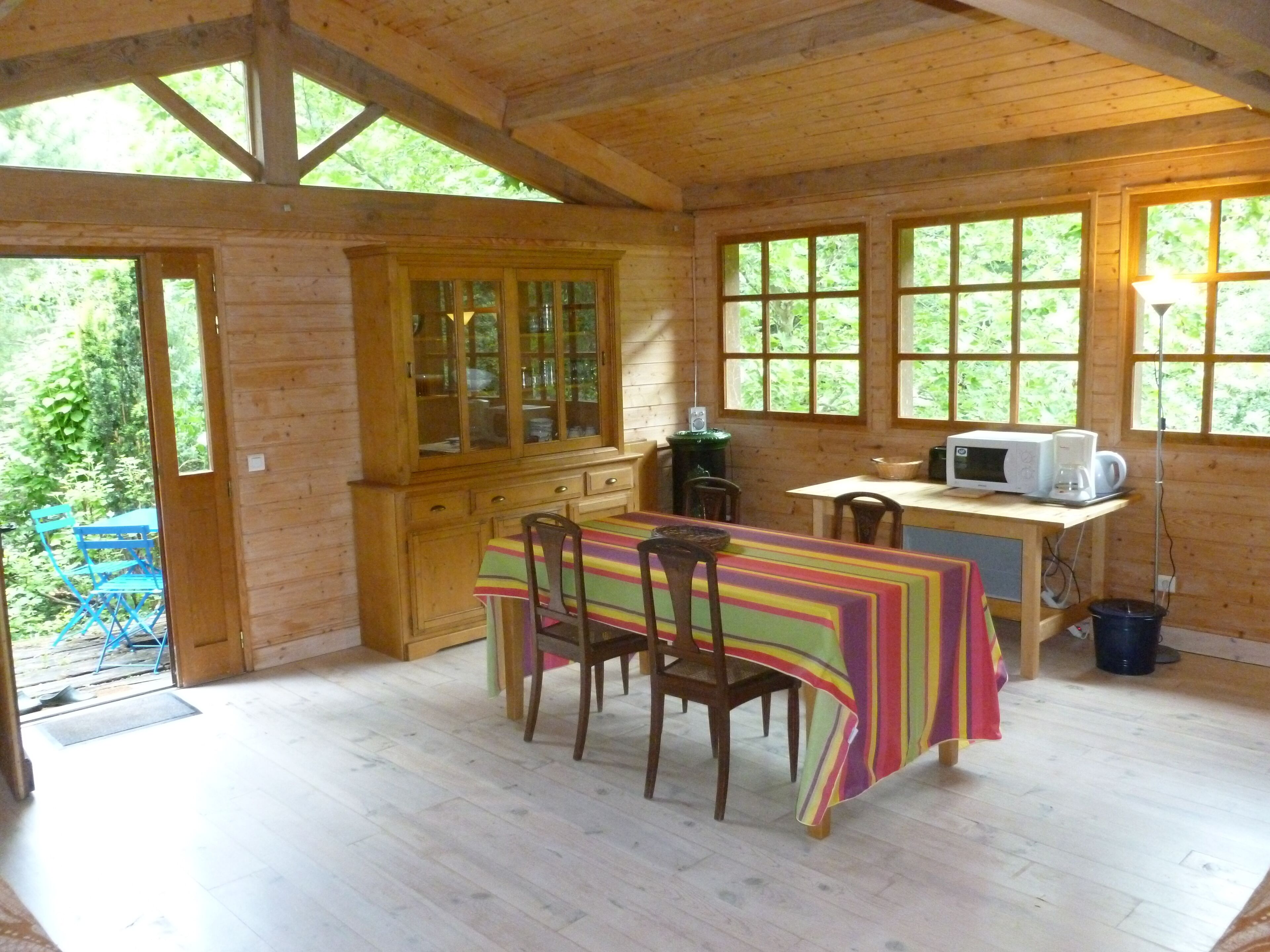 Eine Holzhütte mit Essbereich, inklusive Tisch mit Stühlen, einem Schrank mit Glastüren und einer Mikrowelle auf einer Arbeitsplatte.