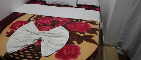 A bed with a floral bedspread, white pillows, and a white towel on the side.