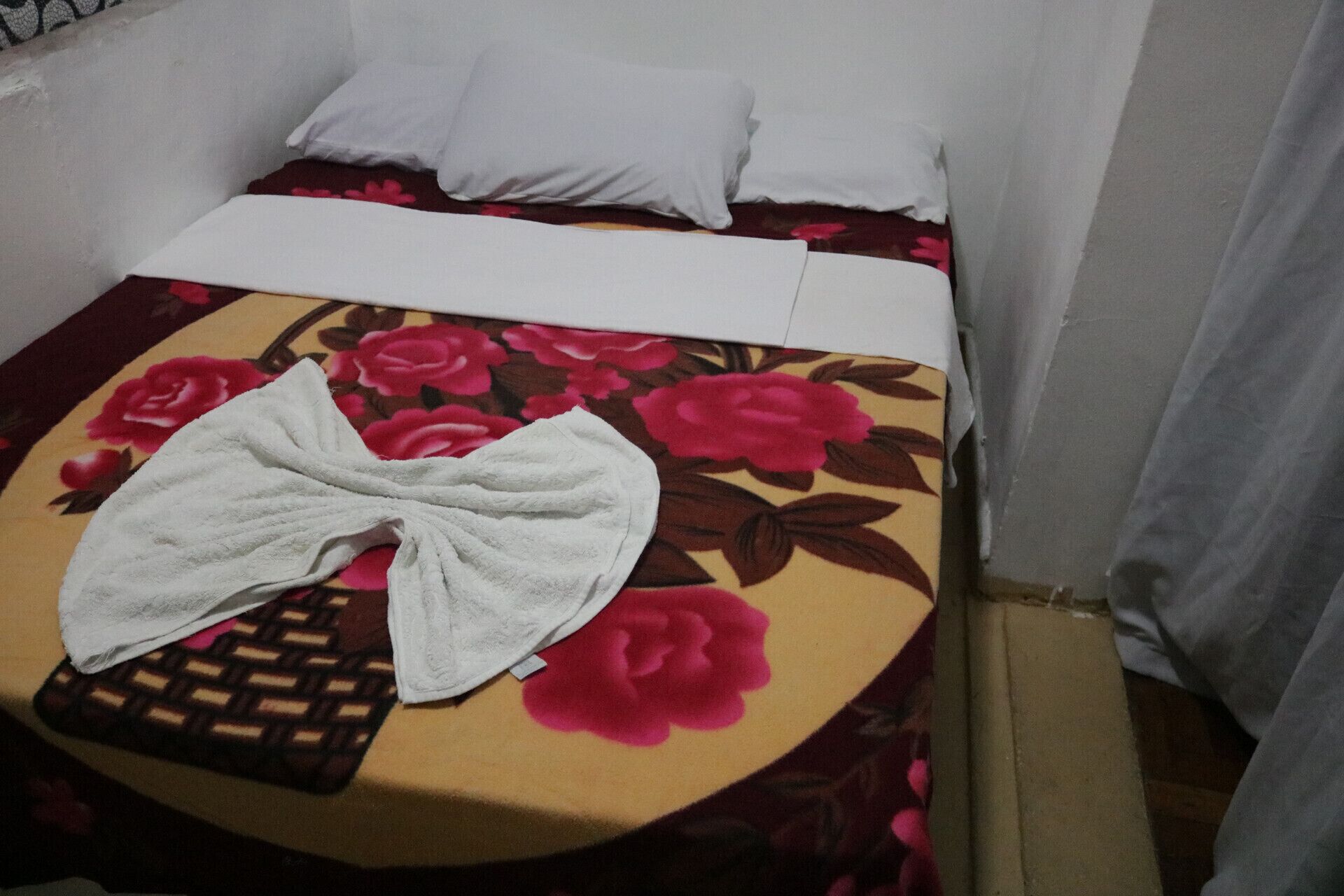 A bed with a floral bedspread, a white pillow, and a white towel on a small table.