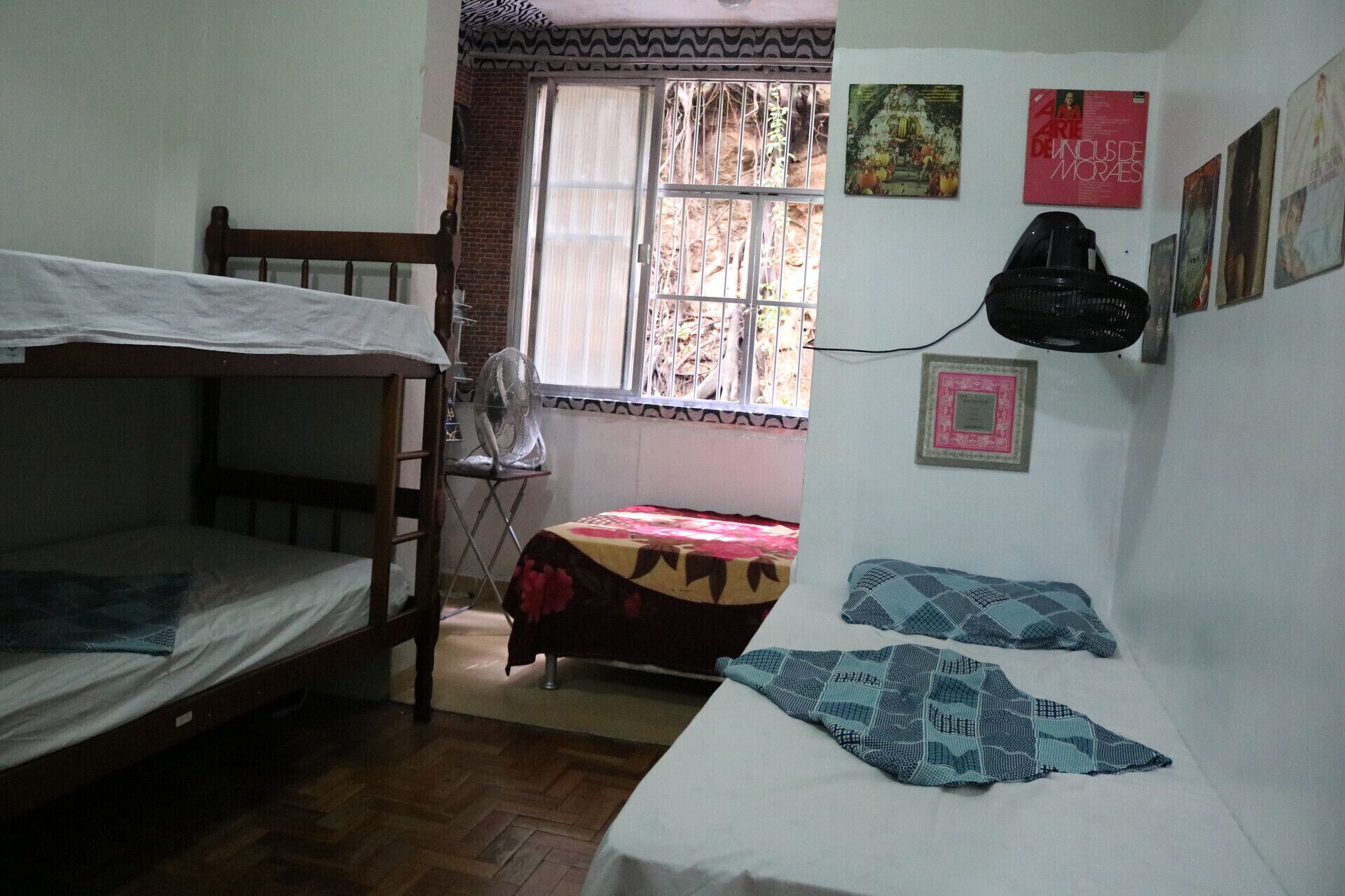 A dormitory room with bunk beds, a fan, a window with bars, and wall decorations.