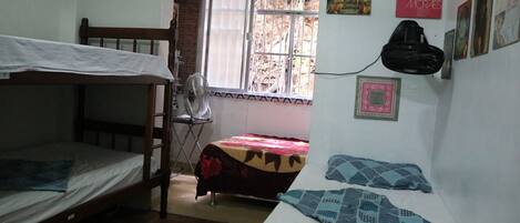 A dormitory room with bunk beds, a fan, a window with bars, and wall decorations.