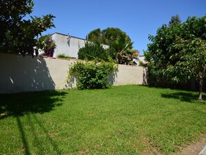 A grassy yard with a low wall, trees, and a building in the background.