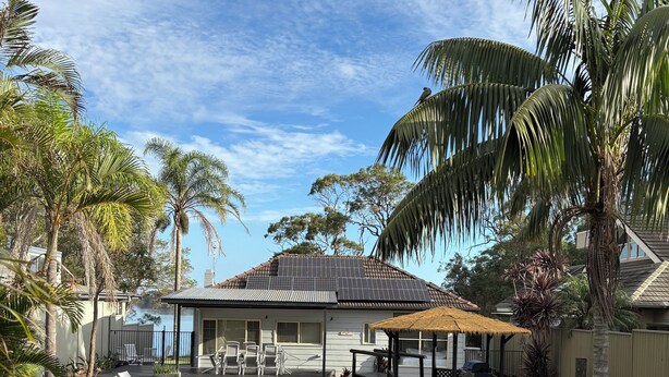 A backyard with a swimming pool, lounge chairs, a barbecue area, and a house with a tiled roof.