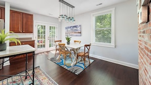 A spacious kitchen with wooden cabinets, a dining area with a white table and chairs, and large windows with blinds. - Renovated 2B w/Balcony by OTR, UC, Findlay Market (Cincinnati)