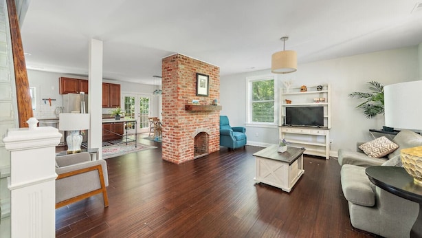 A spacious living room with hardwood flooring, a brick fireplace, a television, and a comfortable seating area. - Renovated 2B w/Balcony by OTR, UC, Findlay Market (Cincinnati)