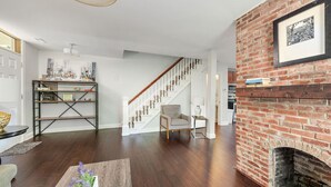 A spacious living room with hardwood flooring, a fireplace, a staircase, and a bookshelf. - 2 Apts w/ Terrace-OTR, Findlay Market, Rhinegeist (Cincinnati)