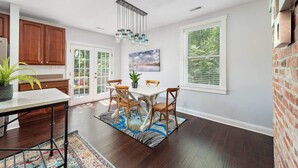 A spacious kitchen with wooden cabinets, a dining area with a white table and chairs, and large windows with blinds. - 2 Apts w/ Terrace-OTR, Findlay Market, Rhinegeist (Cincinnati)