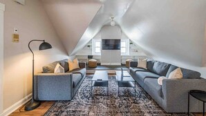 A modern loft-style living room with a high ceiling, two grey sofas, a coffee table, and a floor lamp.