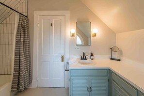 Une salle de bain avec une porte blanche, un rideau de douche à rayures, un lavabo avec un miroir et deux appliques murales.