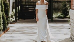 Eine Person in einem weißen Kleid steht im Freien, mit einem Gebäude und Bäumen im Hintergrund.