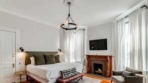 Ein Schlafzimmer mit einem großen Bett, einem Kamin, einem Fernseher und einem Sessel.