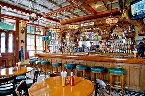 A bar with wooden bar stools, a counter with bottles, and a sign that reads "No Sniveling".