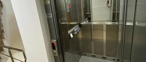 Un ascenseur doté d’un écran numérique, d’un intérieur métallique et d’une porte en verre.