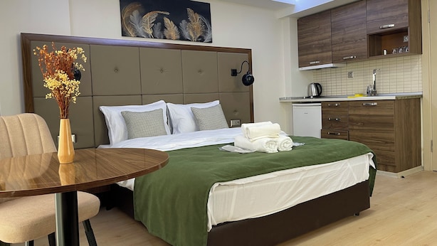 Une chambre d’hôtel moderne comprenant un lit, une table à manger, un vase avec des fleurs séchées, un tableau au mur et un coin cuisine.